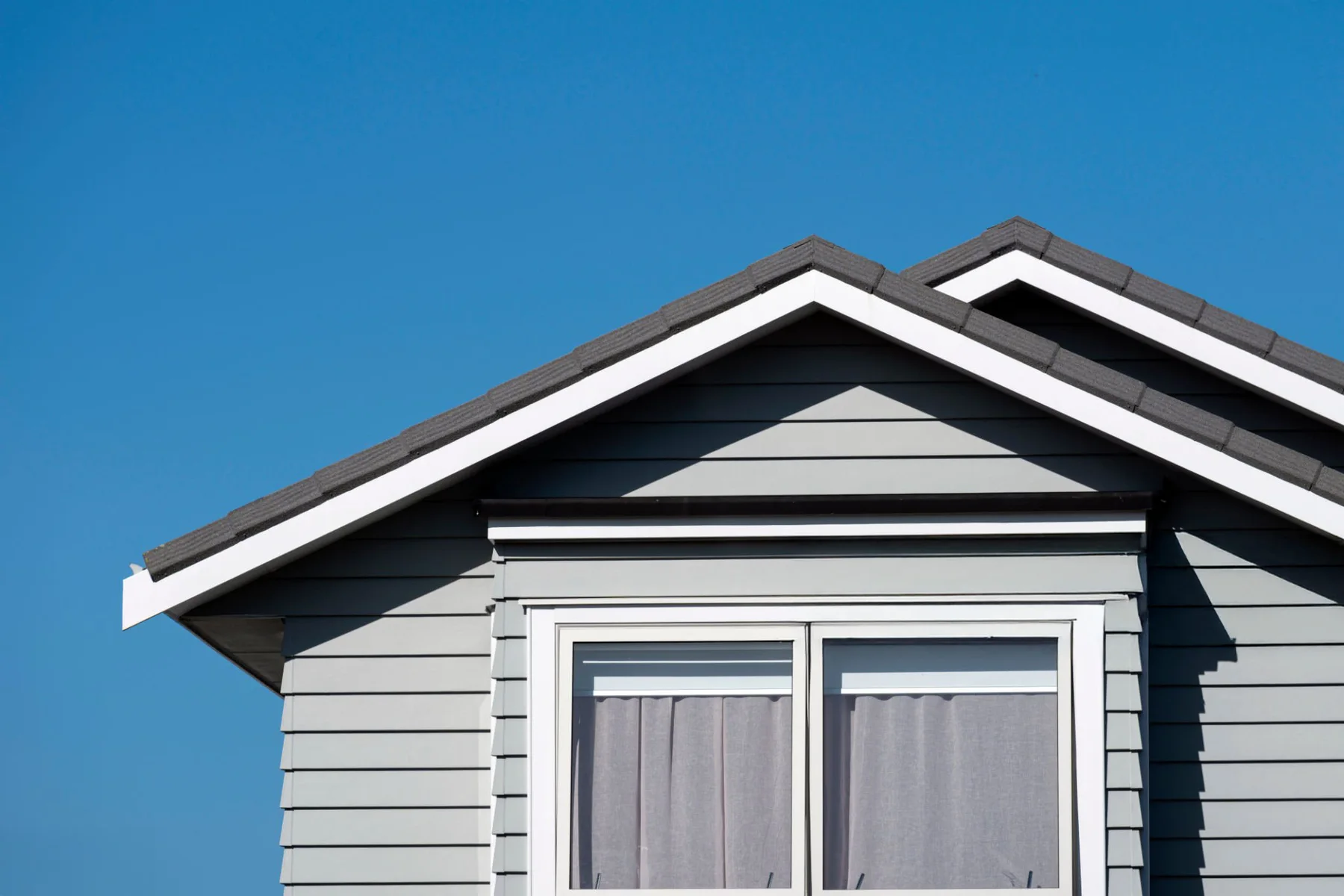 Grey weatherboard home with gabled roof against a clear blue sky in Auckland